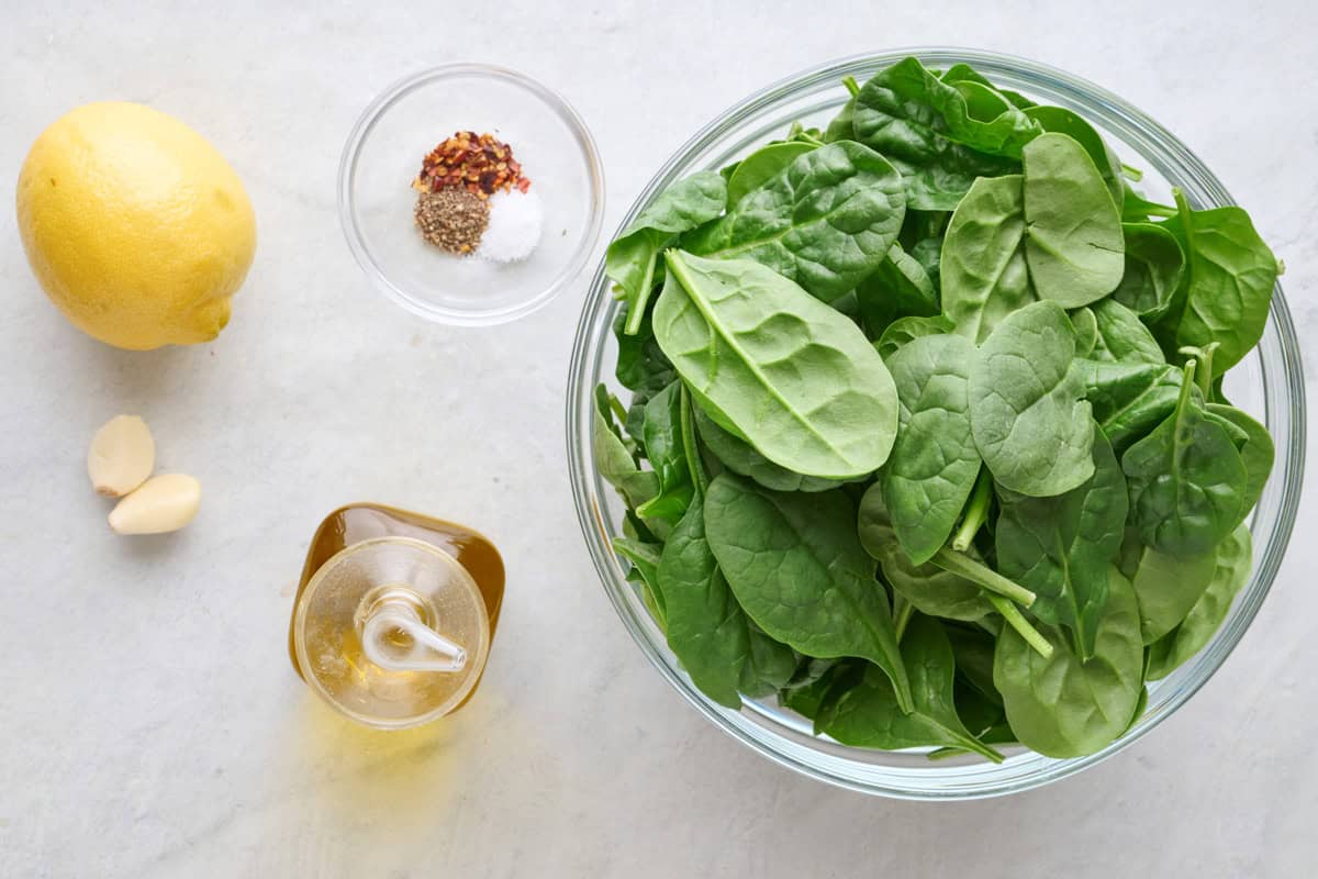 Ingredients for recipe: lemon, garlic, spices, oil, and fresh spinach.