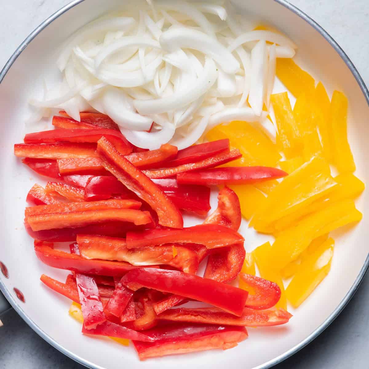 Sliced peppers and onions in a skillet before cooking.