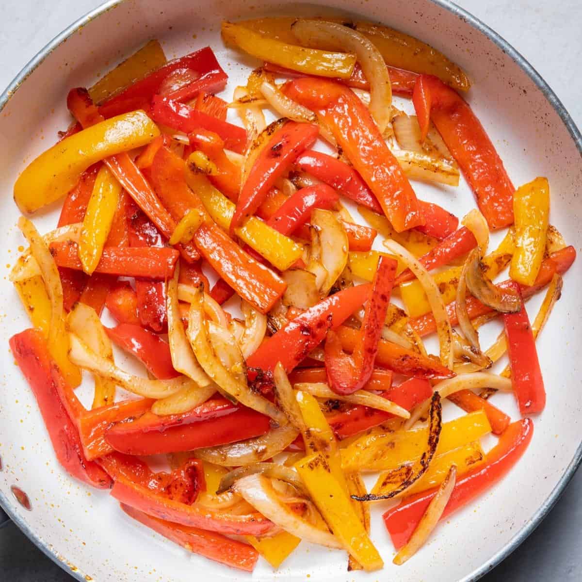 Sliced peppers and onions in a skillet after cooking.