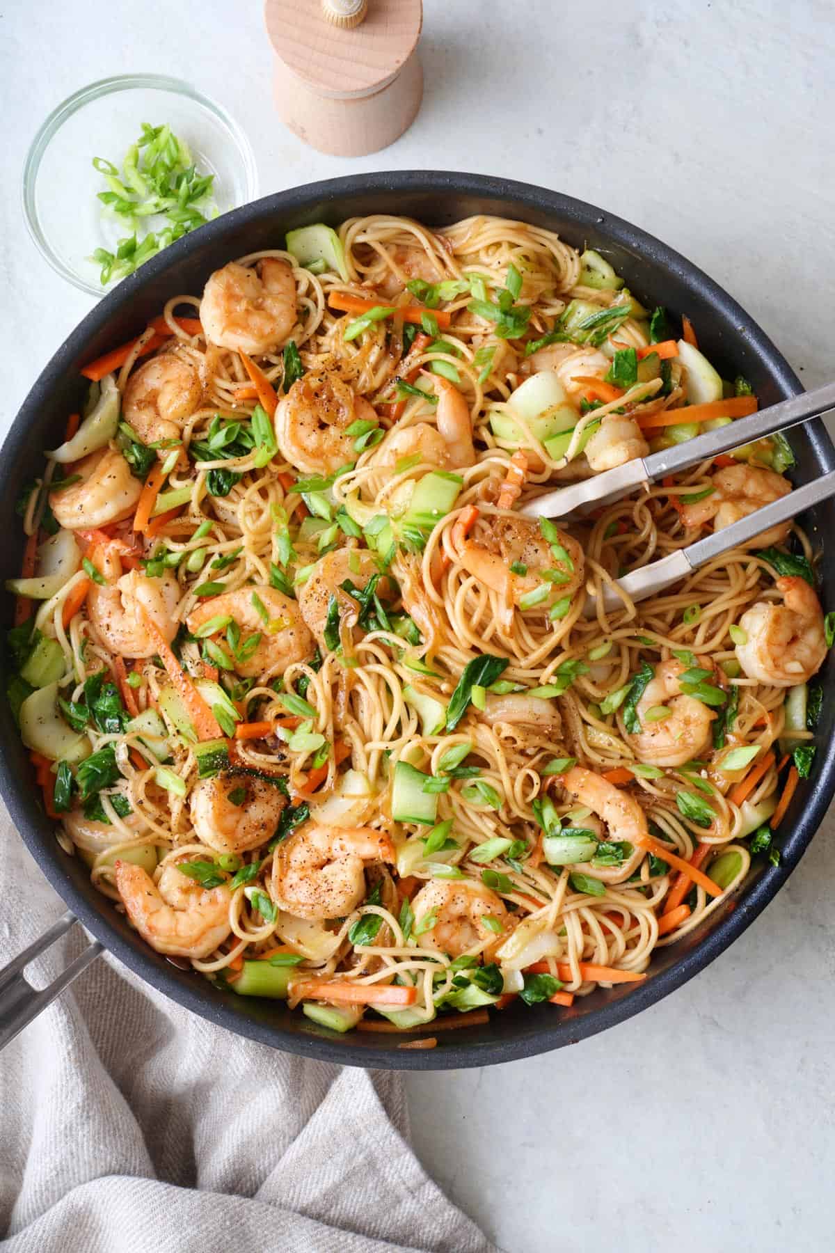 Shrimp lo main in skillet garnished with green onions and tongs and green onions nearby.