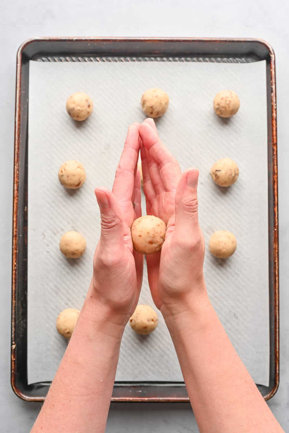 Hand rolling a cookie dough ball over baking sheet with some already rolled.