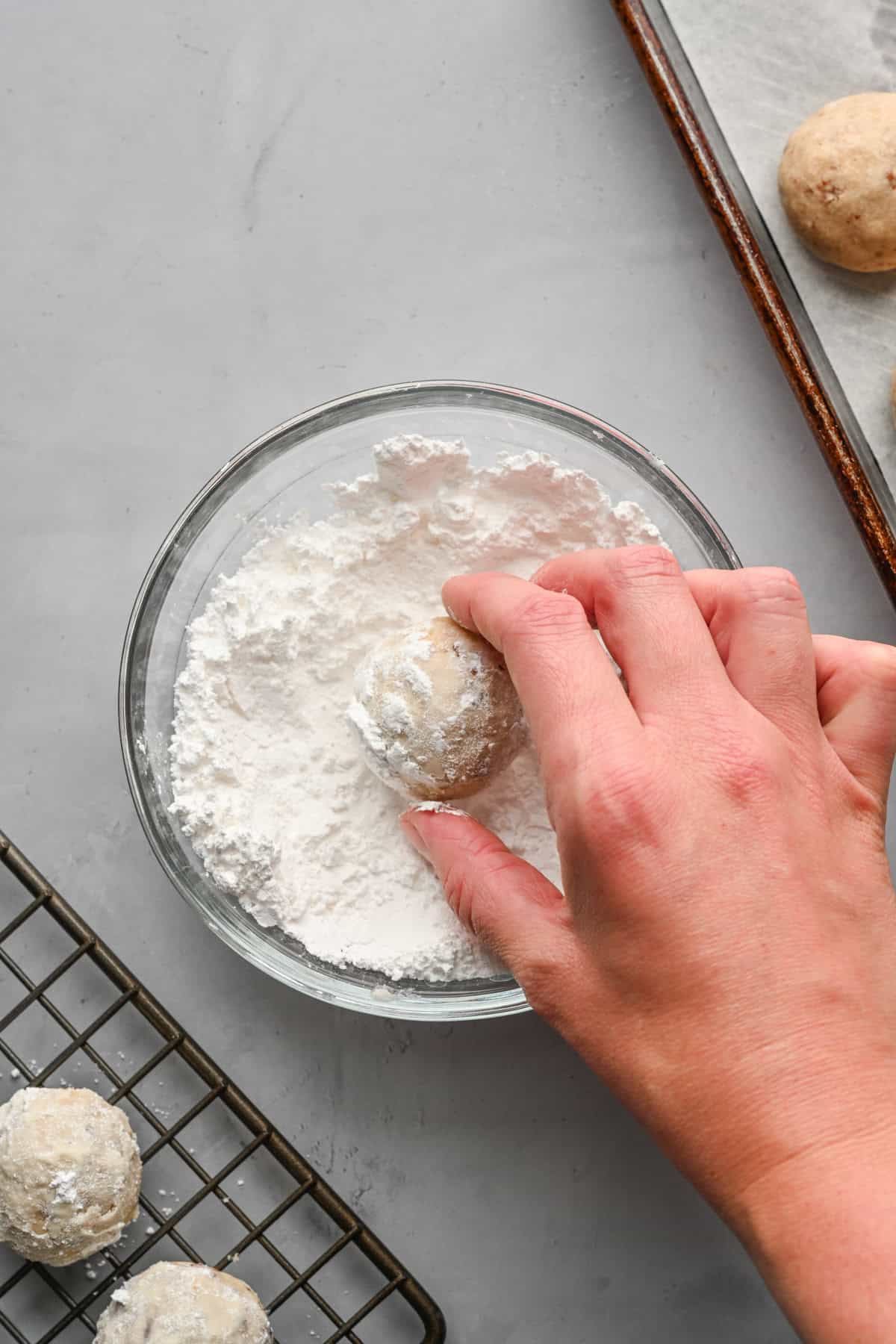 Rolling baked cookies in remaining powdered sugar with tray nearby.