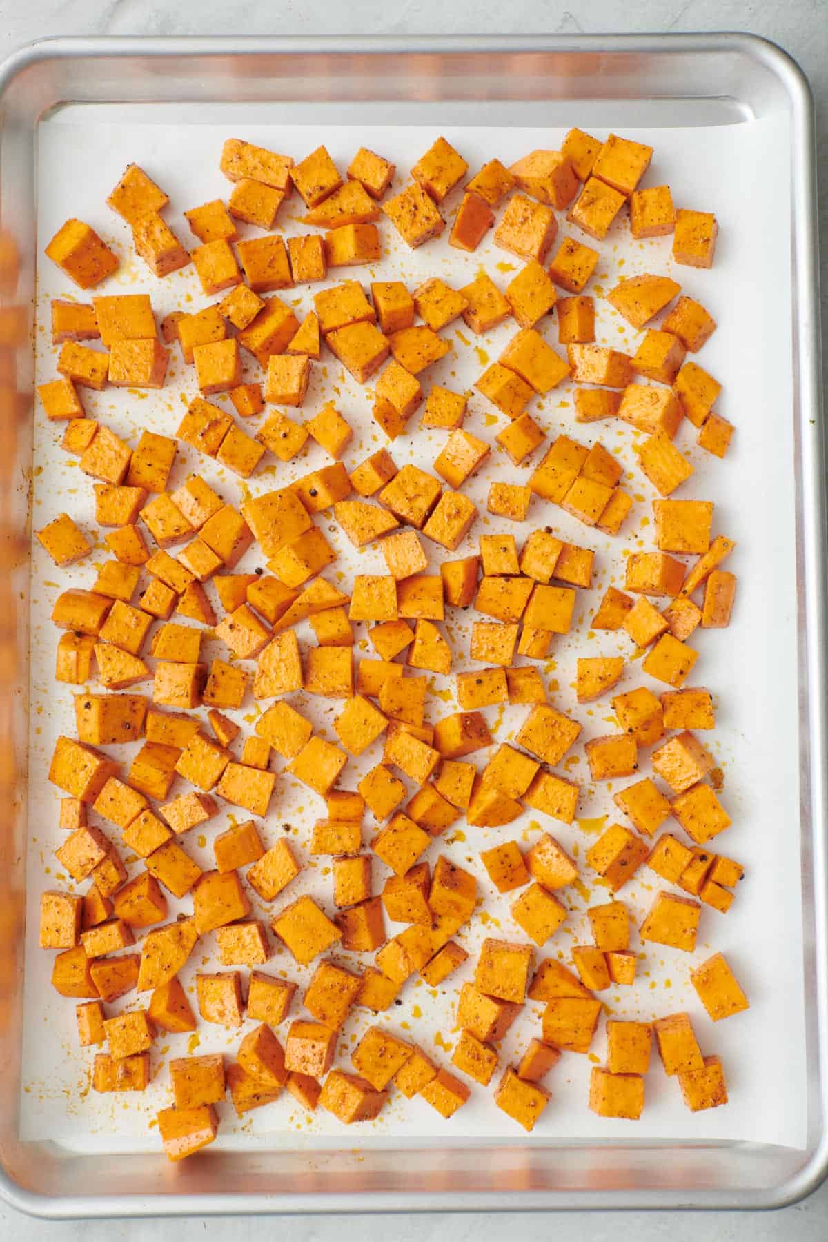 Diced sweet potatoes on a parchment lined baking sheet with oil and spices.