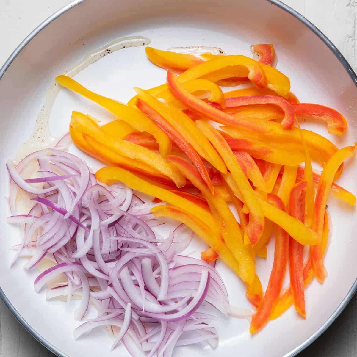 Sliced peppers and onions in a skillet.