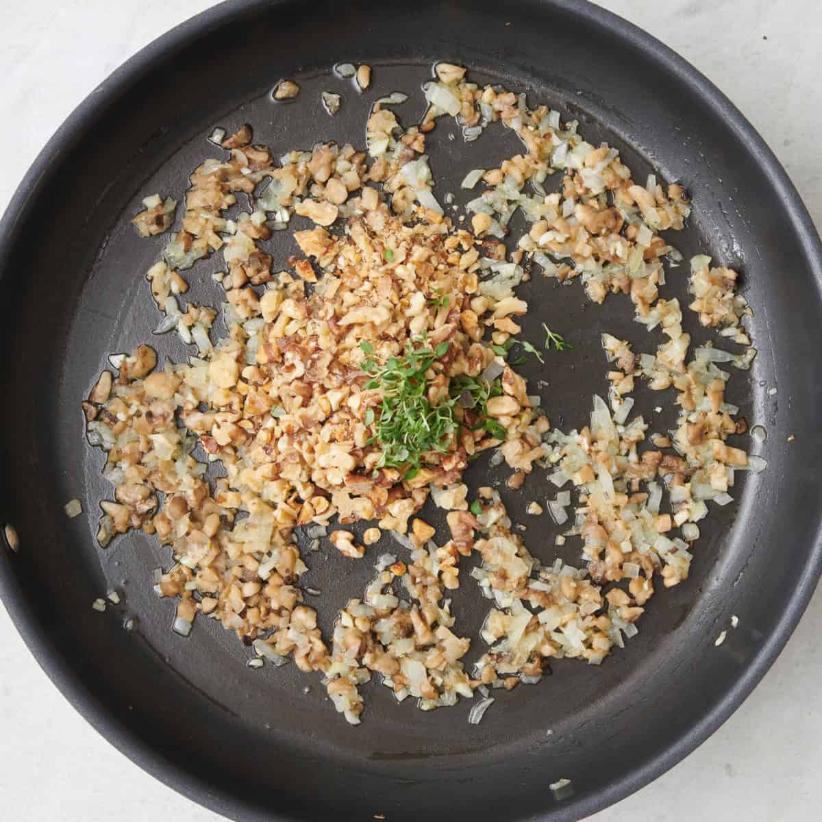 Mushroom pieces and herbs added to cooked onions and garlic mixture.