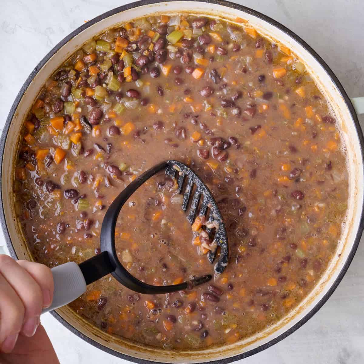 Potato masher in pot mashing soup.