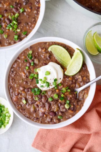 Two bowls of black bean soup with yogurt, lime, and green onions on top.