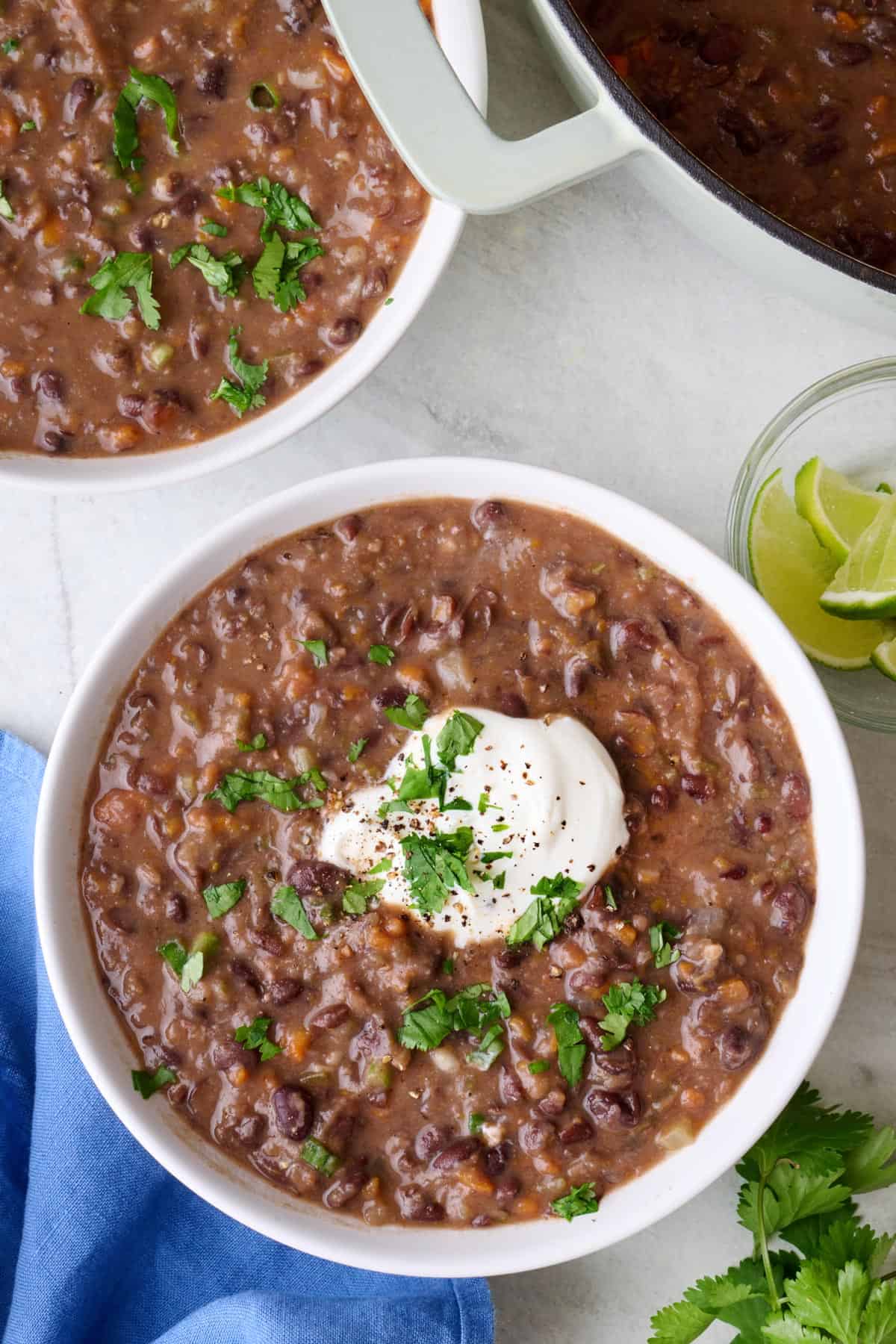 Two bowls of black bean soup, one topped with Greek yogurt and chopped parsley.