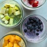 Blended overnight oats in 4 jars with 4 different fresh fruit flavor varieties: apple and spinach, strawberry, mango, and blueberry.