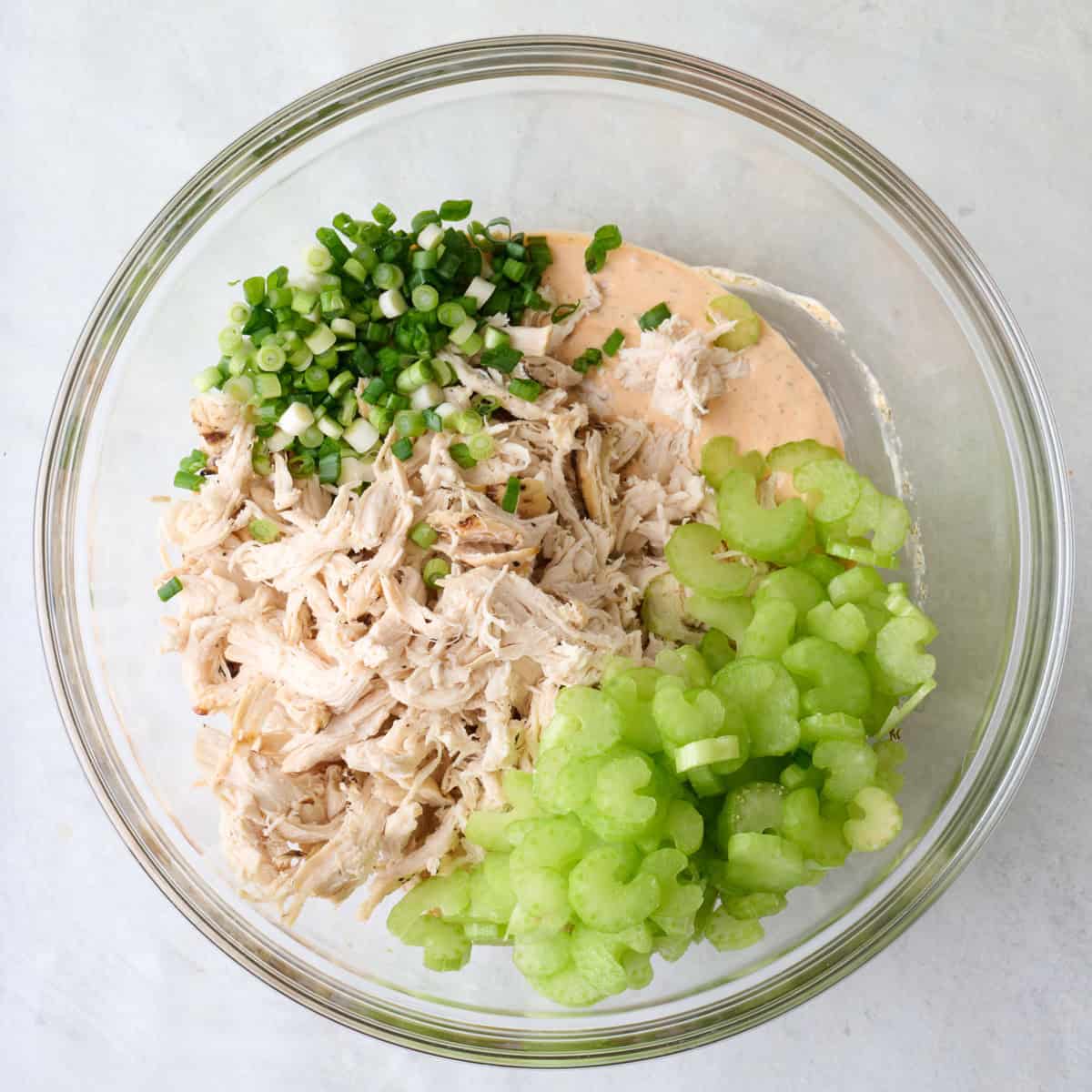 Creamy buffalo sauce in a bowl with shredded chicken, green onions, and celery added on top.