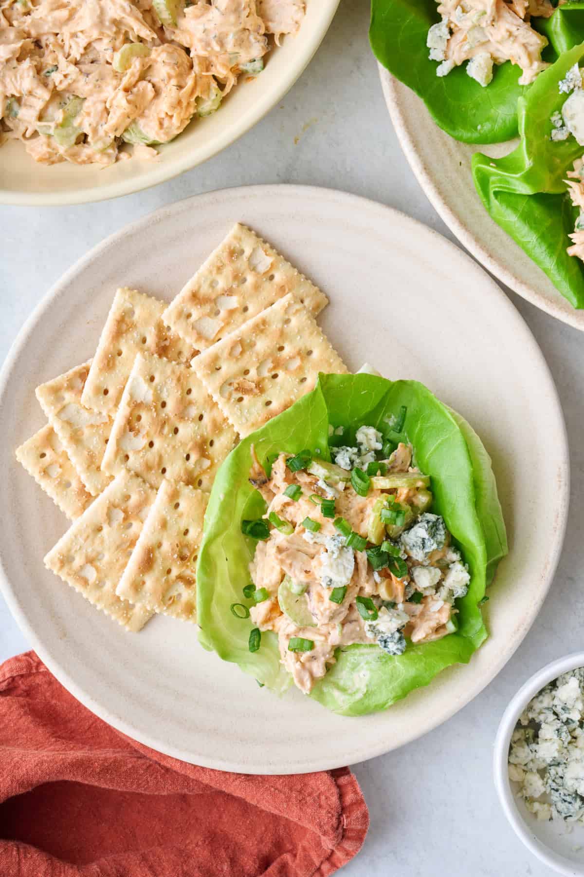 Lettuce cup with shredded buffalo chicken salad on a plate with crackers.