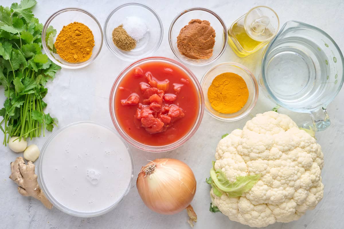 Ingredients for recipe: cilantro, garlic, ginger, turmeric, cumin, salt, red curry paste, curry powder, oil, diced tomatoes, cauliflower, onion, and water.