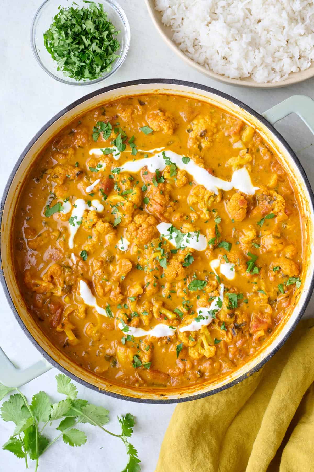 Cauliflower Curry in the pot garnished with extra coconut milk drizzled on and fresh chopped cilantro, bowl of rice nearby.