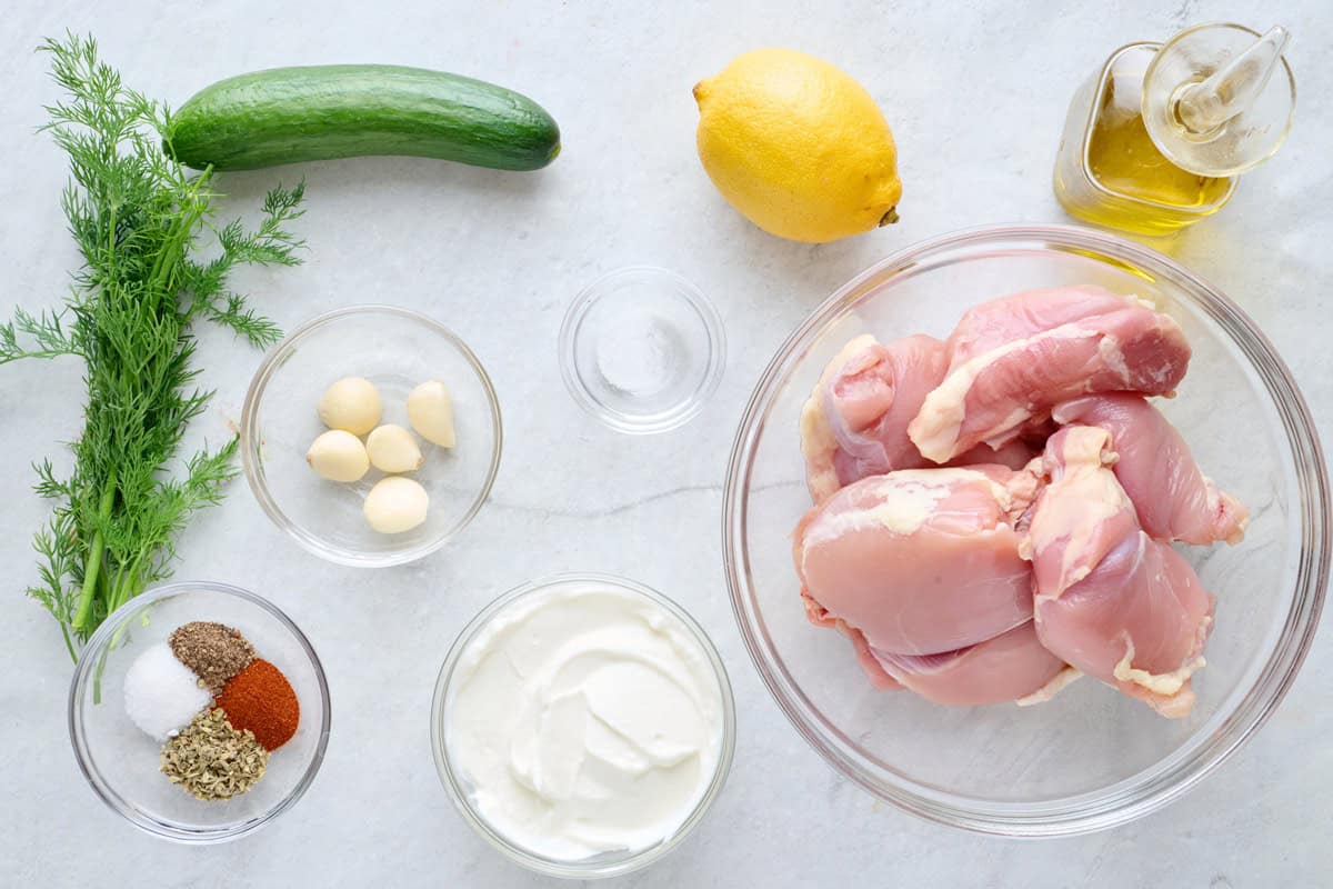 Ingredients for recipe: chicken thighs, oil, lemon, salt, yogurt, garlic, seasonings, cucumber, and dill.