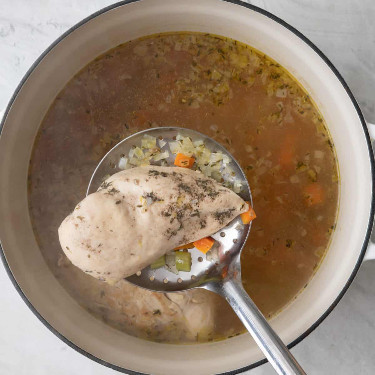 Removing chicken with slotted spoon from the stockpot.