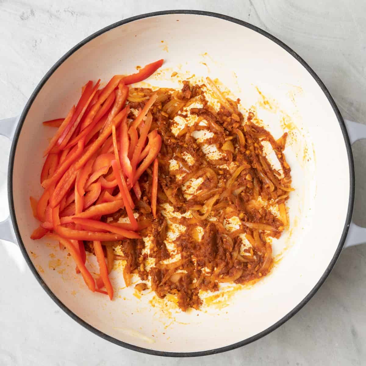 Red curry paste coating the onion mix with red peppers added before mixed.