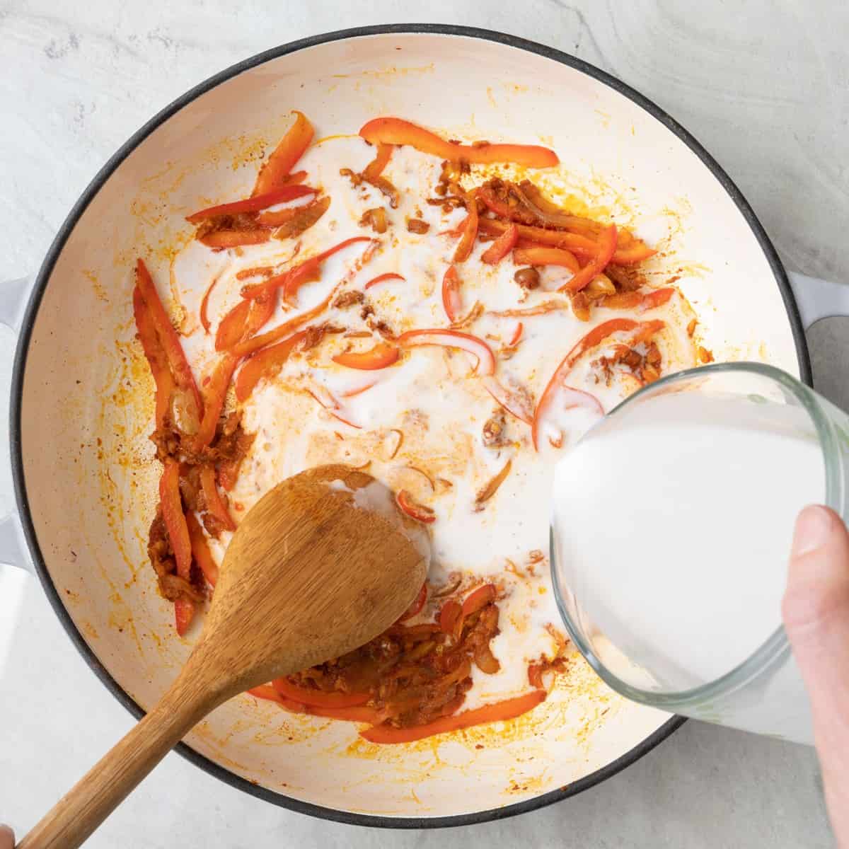 Stirring in coconut milk into spiced veggies.