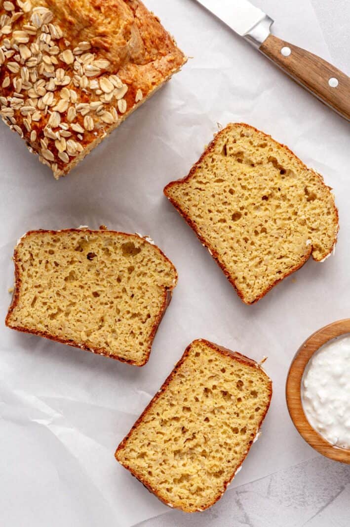 Loat of cottage cheese bread on parchment paper with a few slices cut and laying flat, small dish of cottage cheese nearby.