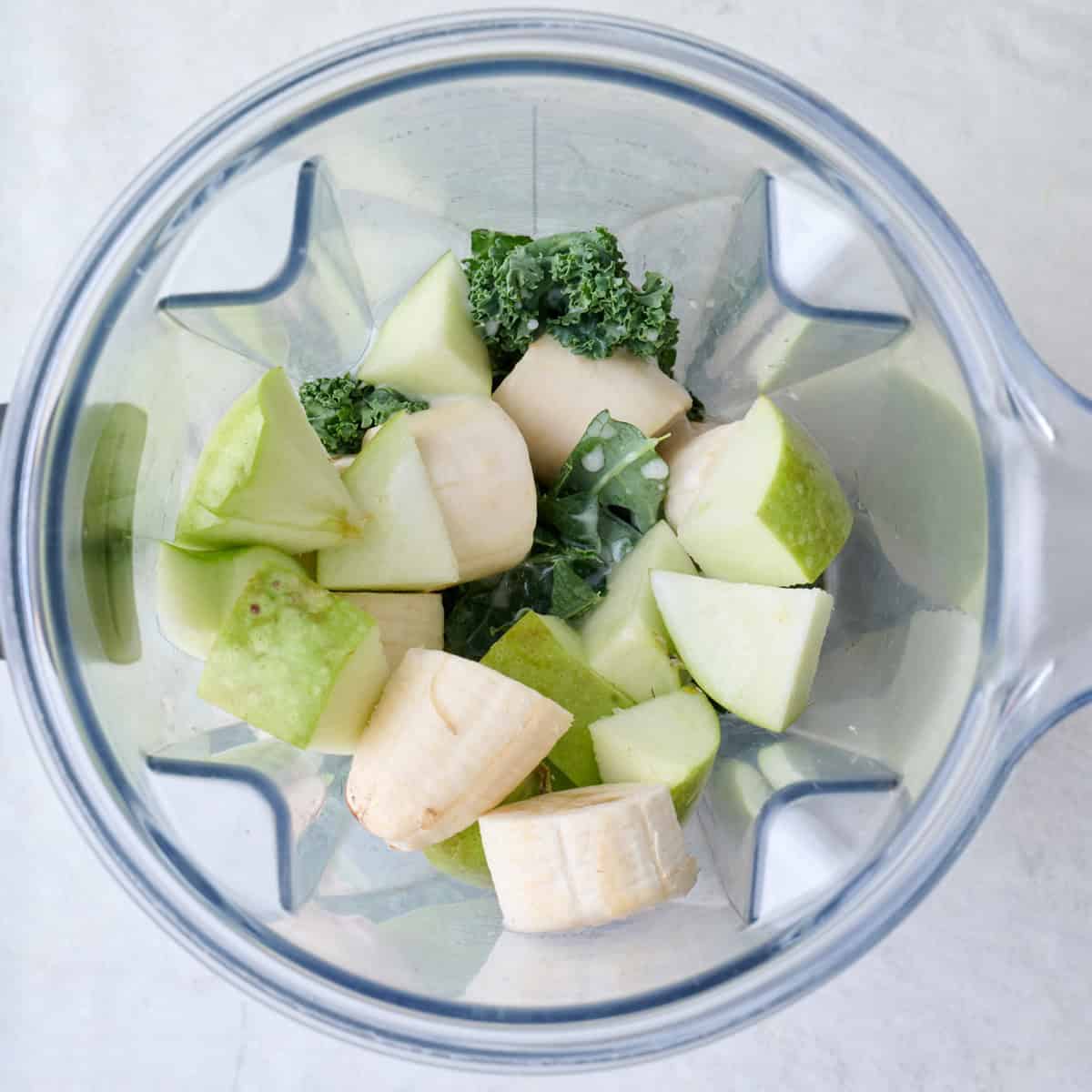 Kale, frozen banana, coconut milk, apple, and ginger in a blender.