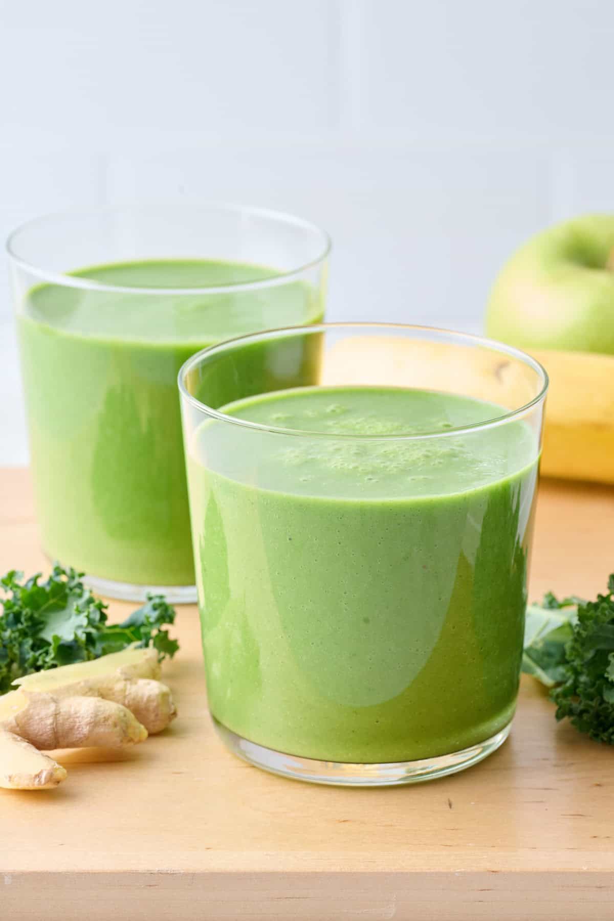 Two glasses of kale smoothie with extra fresh ingredients around.