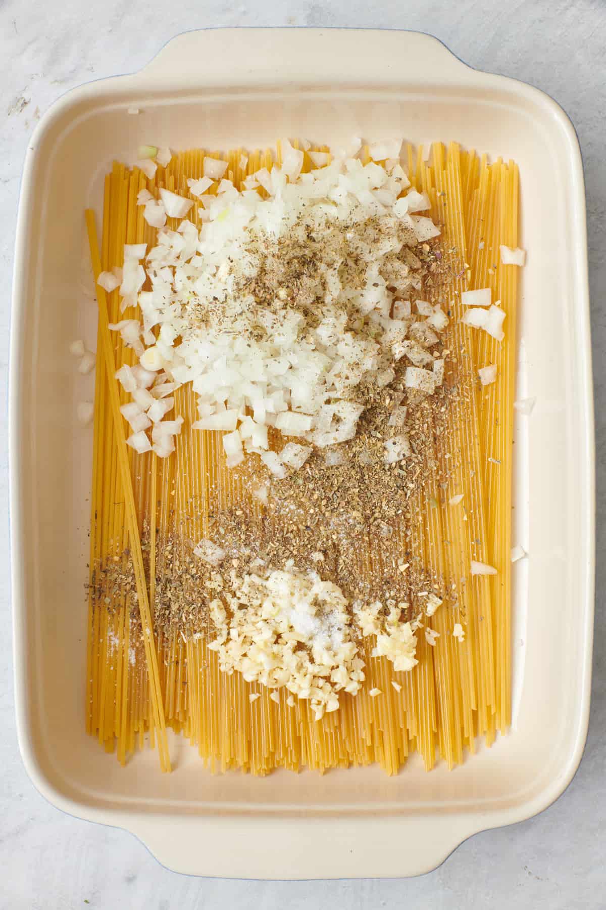 Spaghetti, olive oil, garlic, onions, Italian seasoning, and salt in a baking dish before combining.