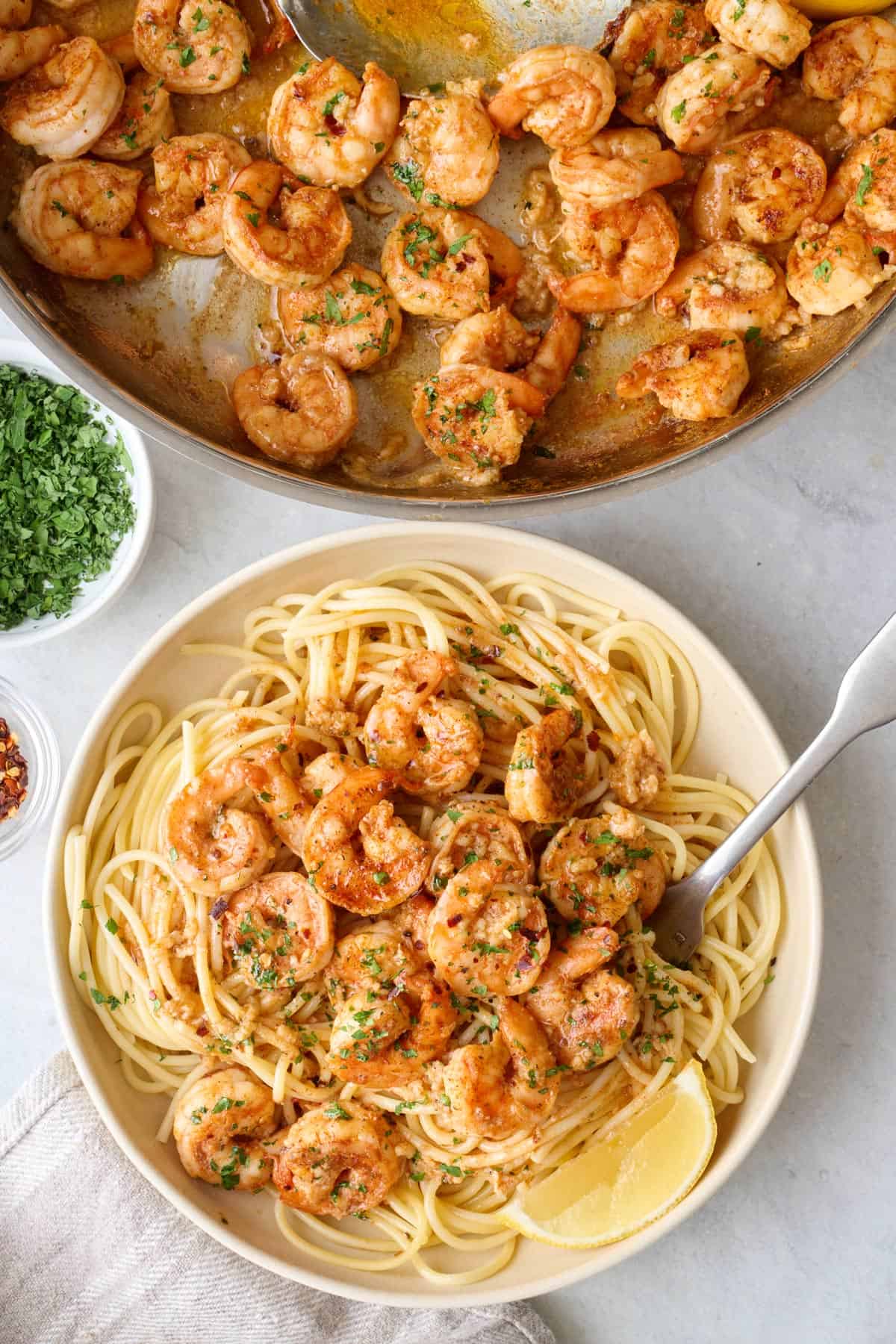 Shrimp served over spaghetti pasta in shallow bowl with lemon and parsley, skillet nearby.