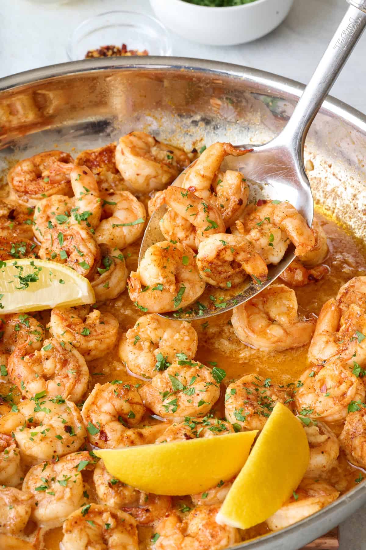 Spoon scooping up some shrimp in garlic butter sauce from pan.