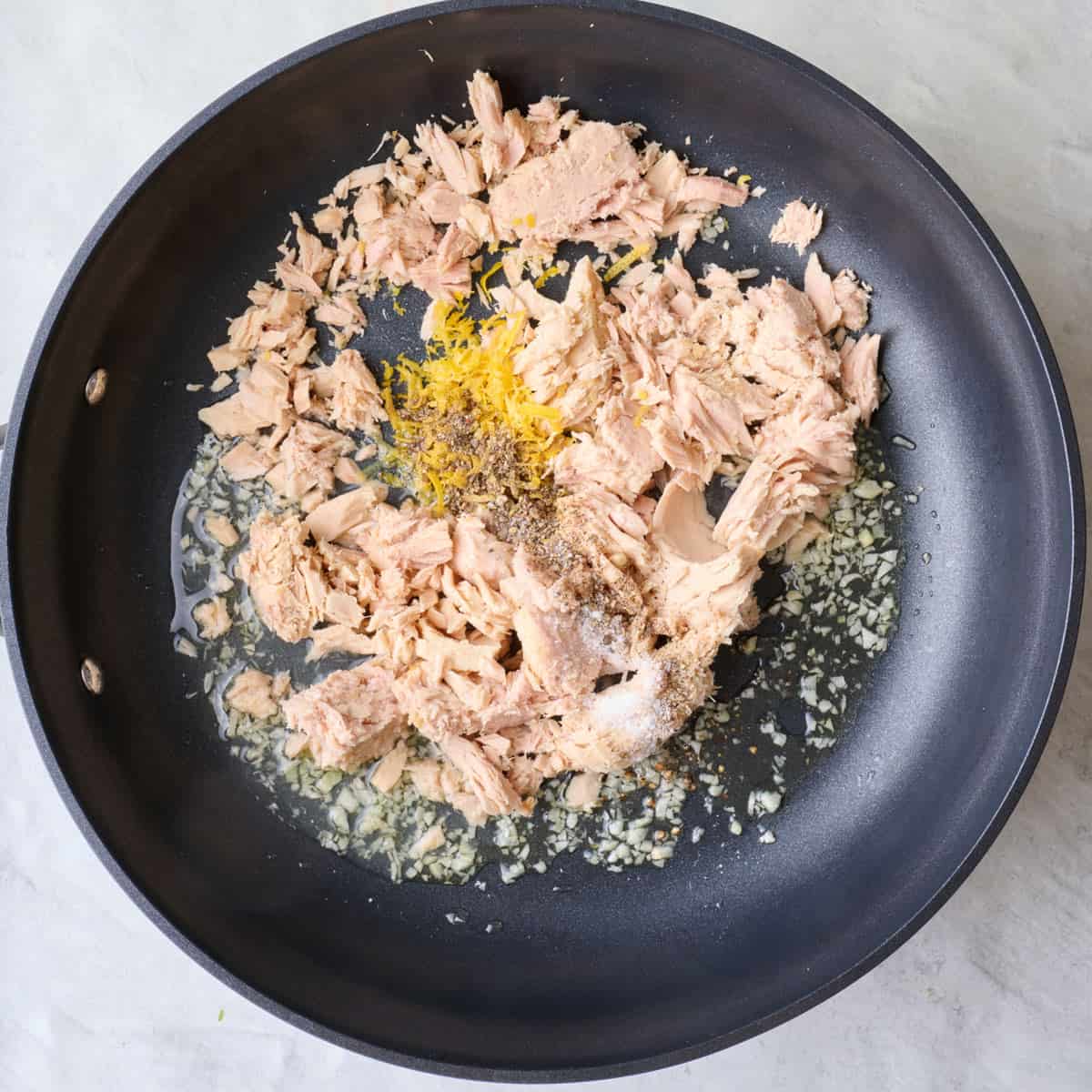 Cooked garlic in pan with canned tuna, zest, juice, salt and pepper added.