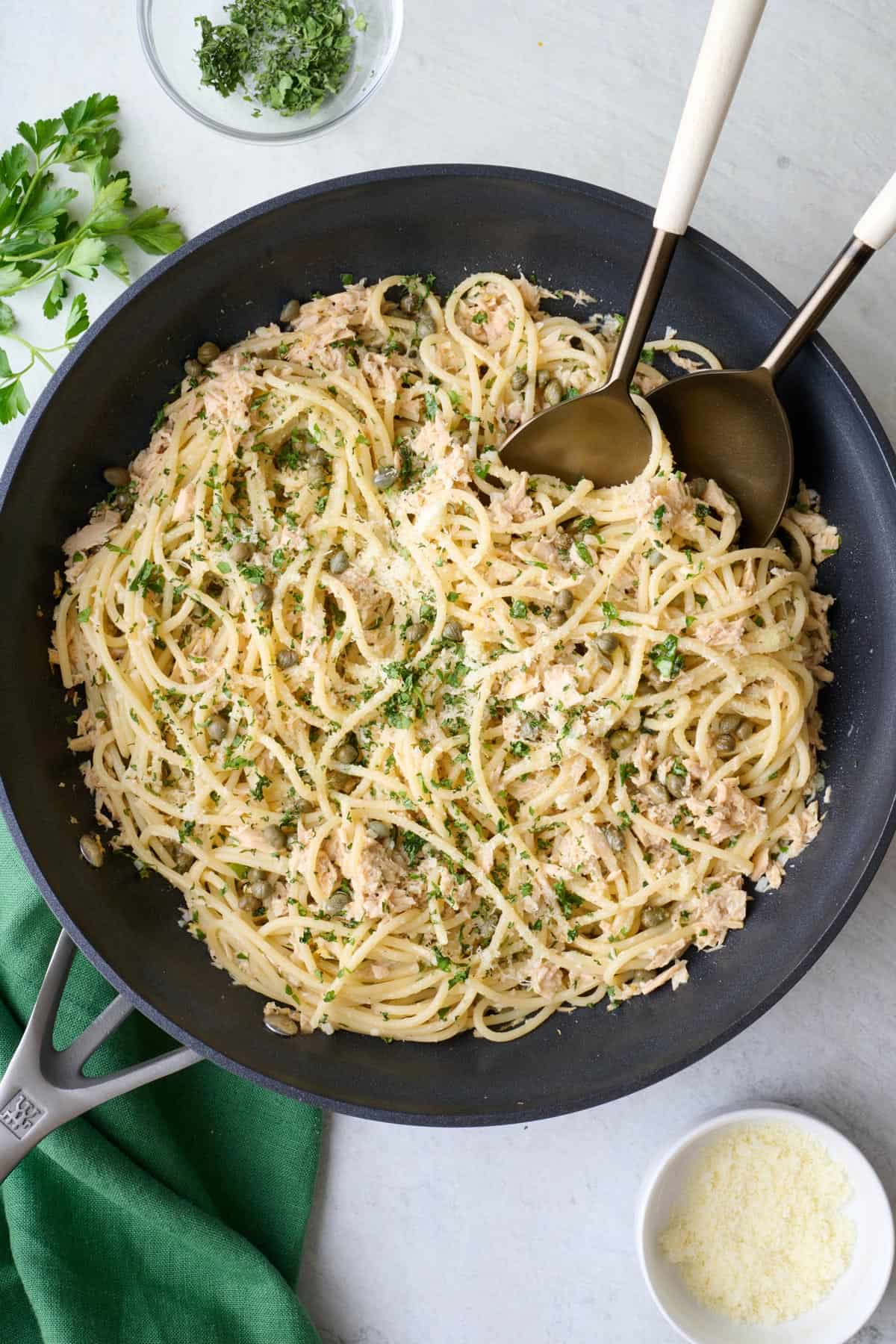 Tuna pasta in shallow pot garnished with fresh parsley and parmesan, serving set dipped inside.