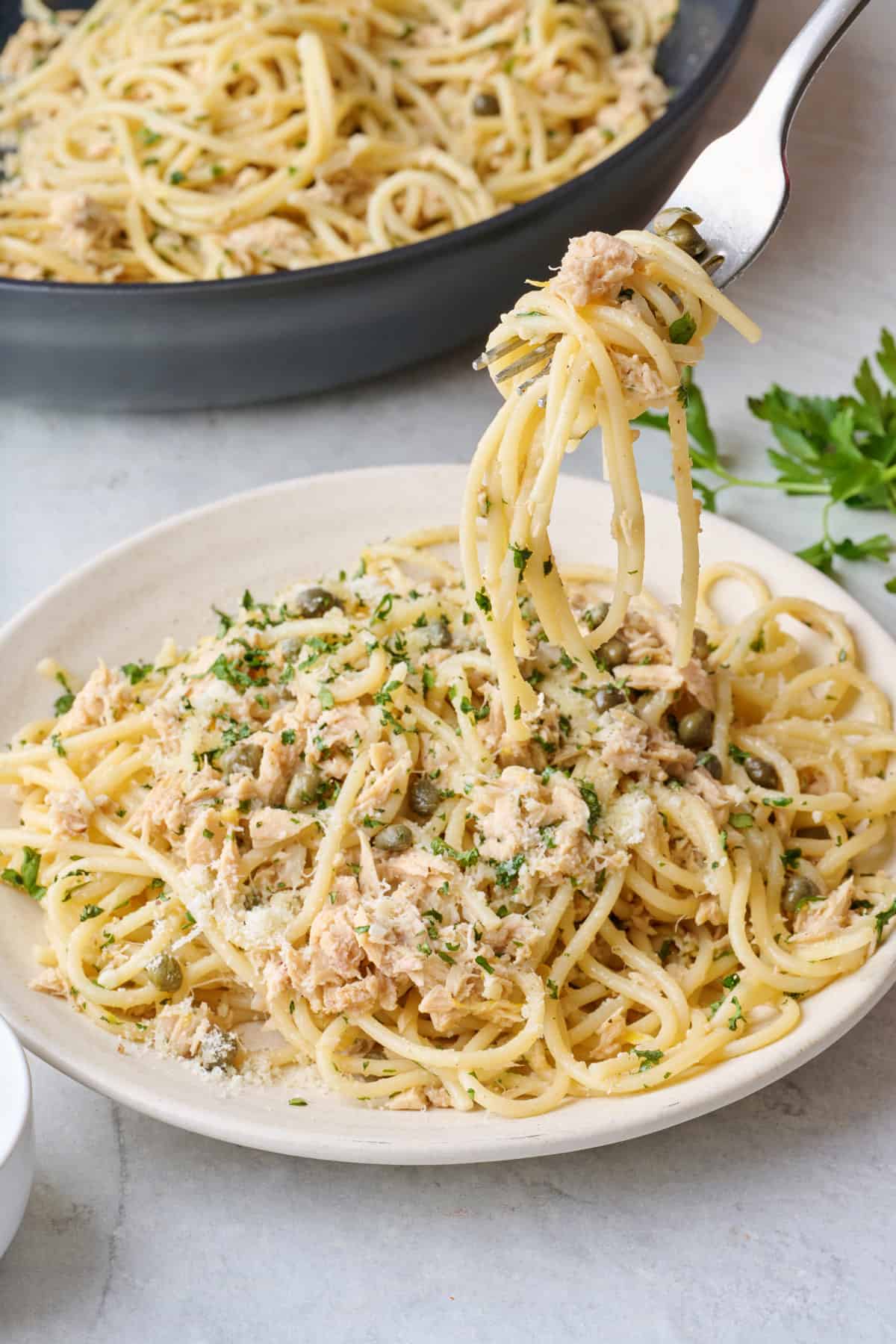 Garlic Lemon Tuna Pasta twirled on fork with hand holding the fork about to pull it out from the plate.