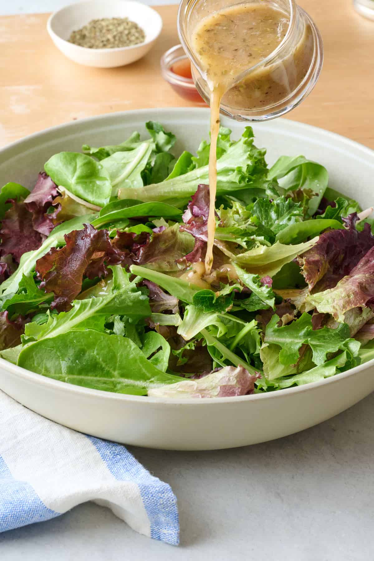 Greek Salad dressing being poured over spring mix.