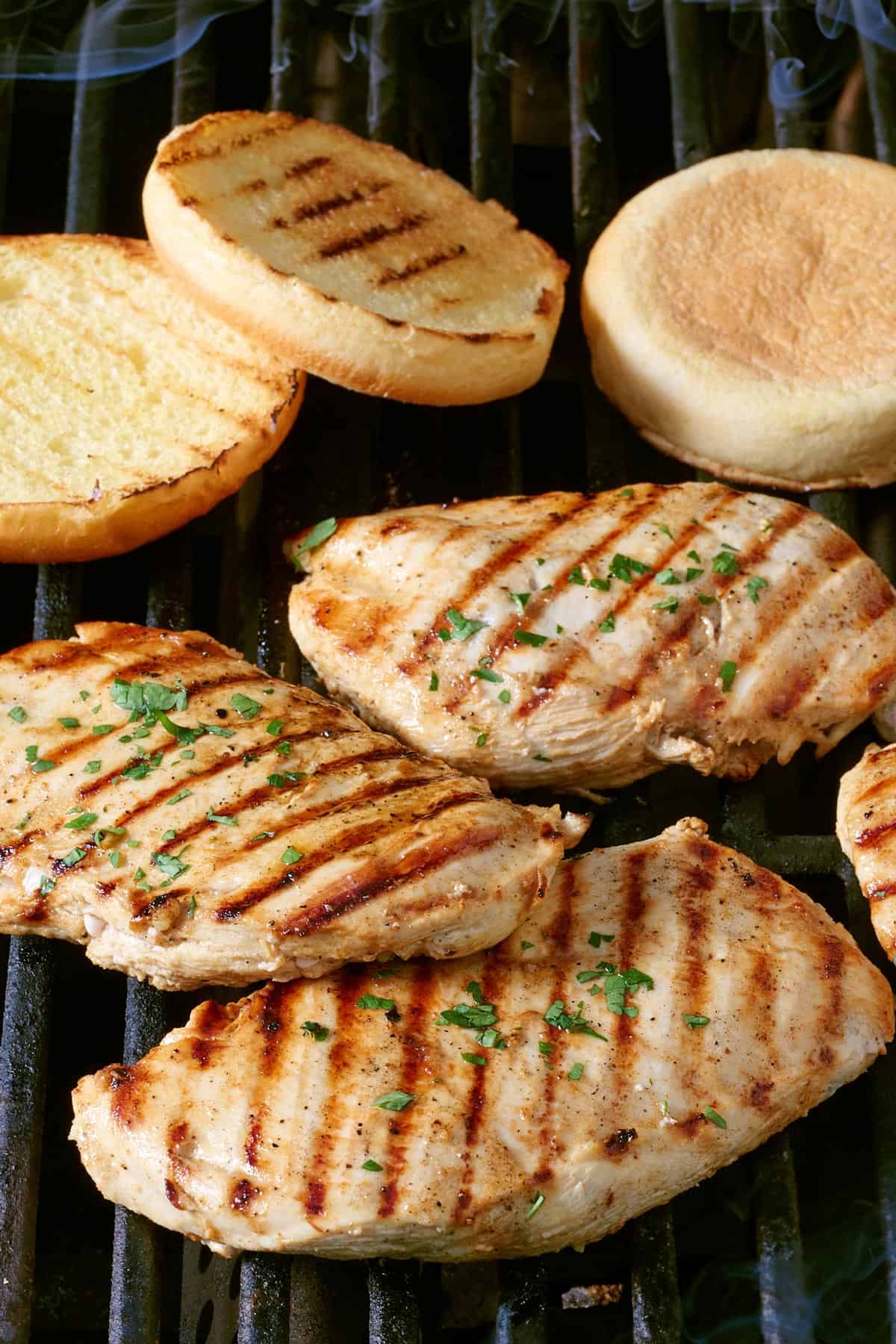 Grilled chicken breasts on grill with a few grilled brioche buns nearby.