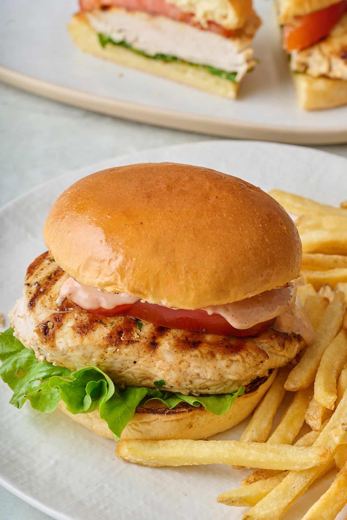 Grilled chicken sandwich on a plate with fries.