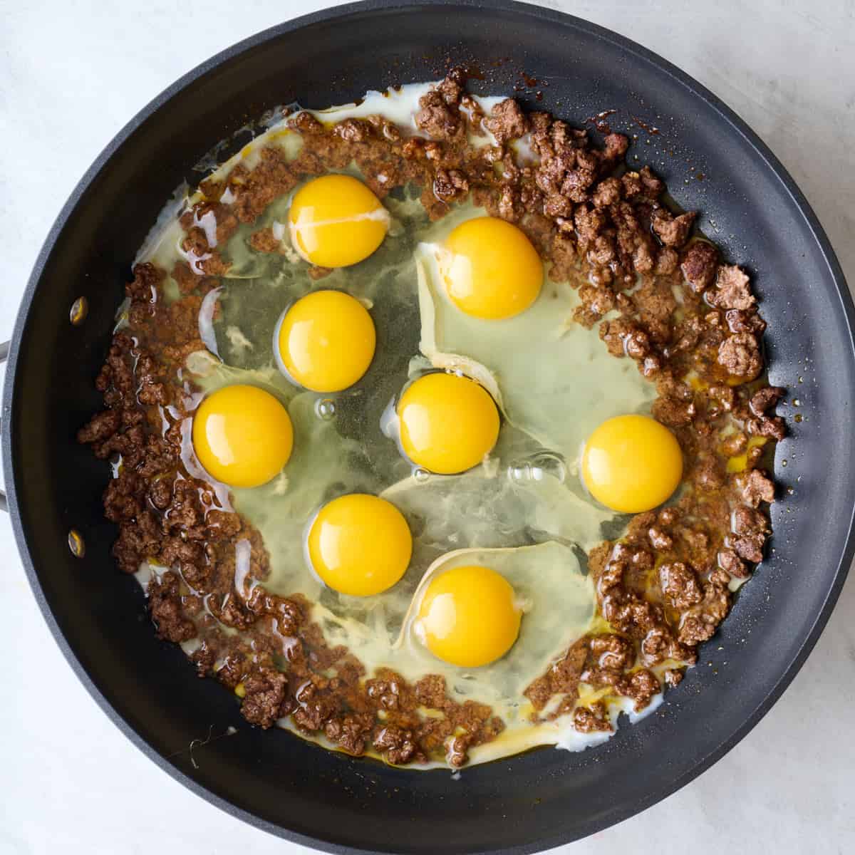 Cooked ground beef in a pan with eggs cracked into it.