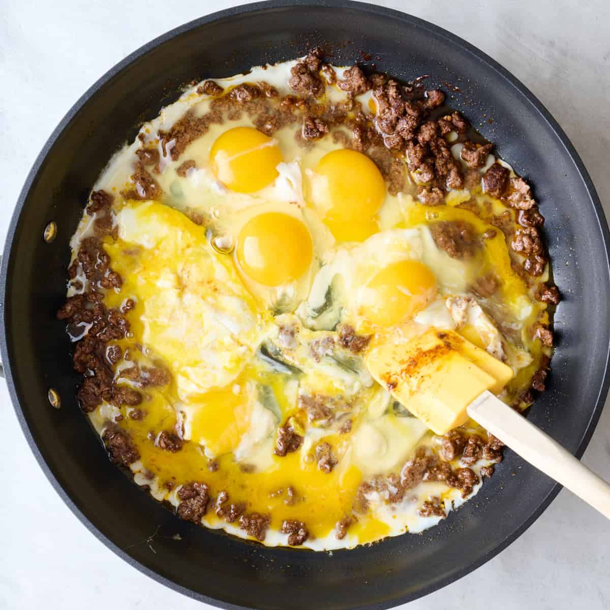 Spatula scrambling partially cooked eggs into ground beef.