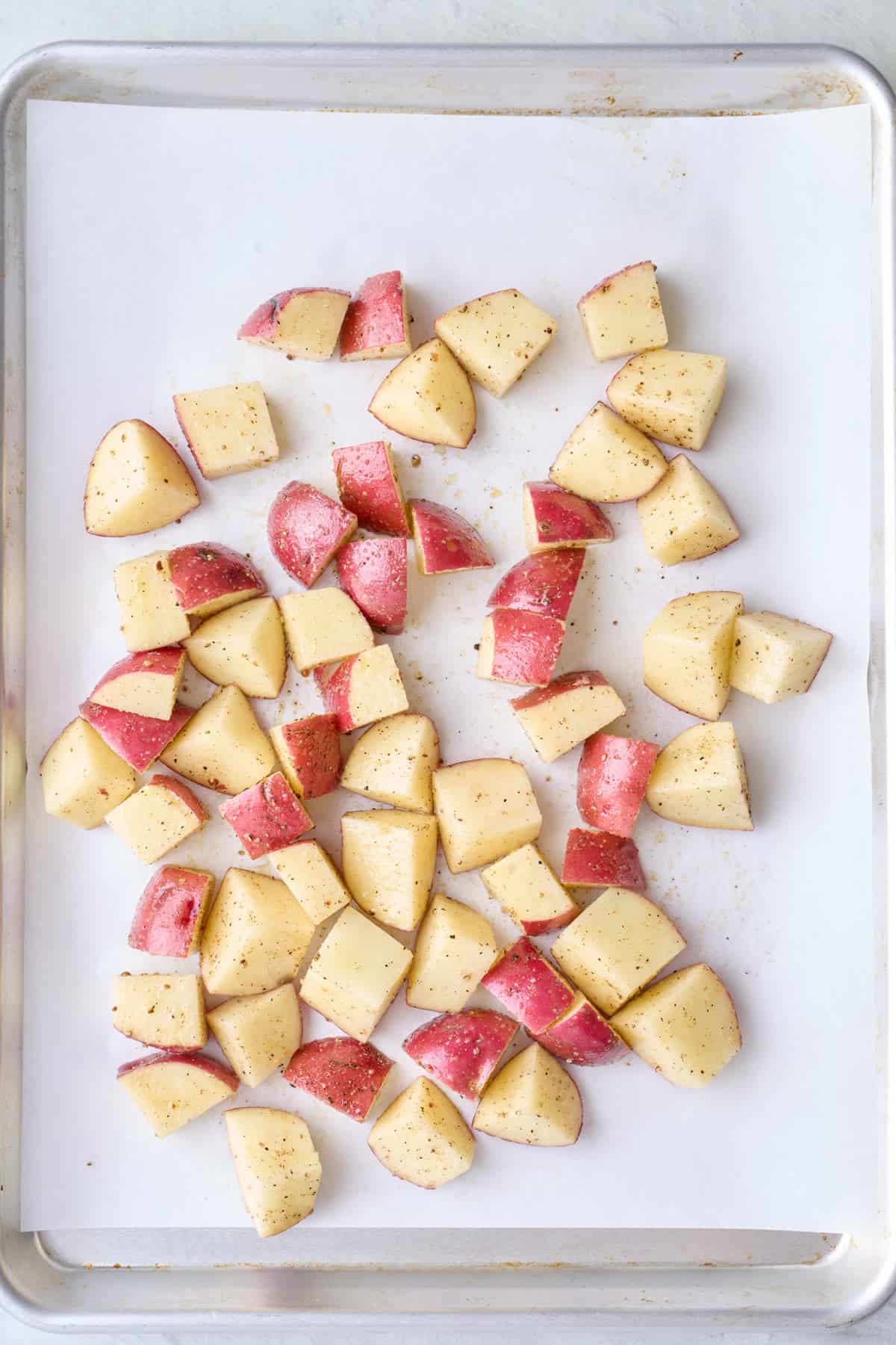 Seasoned red skin potatoes cut into cubes on a parchment lined baking sheet.