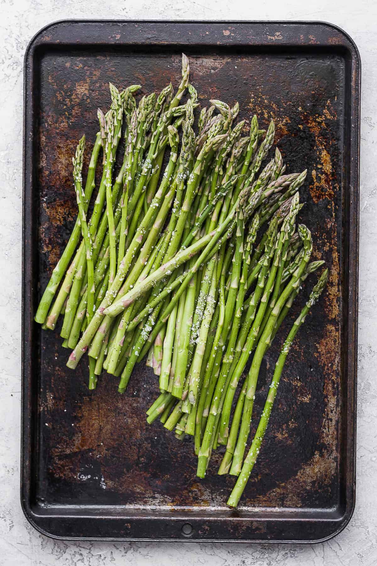 Trimmed asparagus on a sheet pan seasoned with oil, salt and pepper.