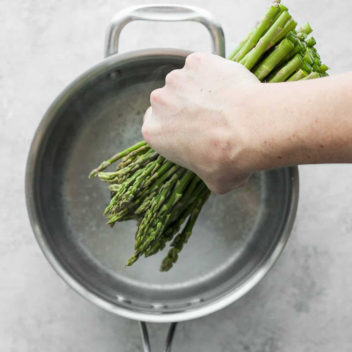 Hand adding asparagus to a pot of water.