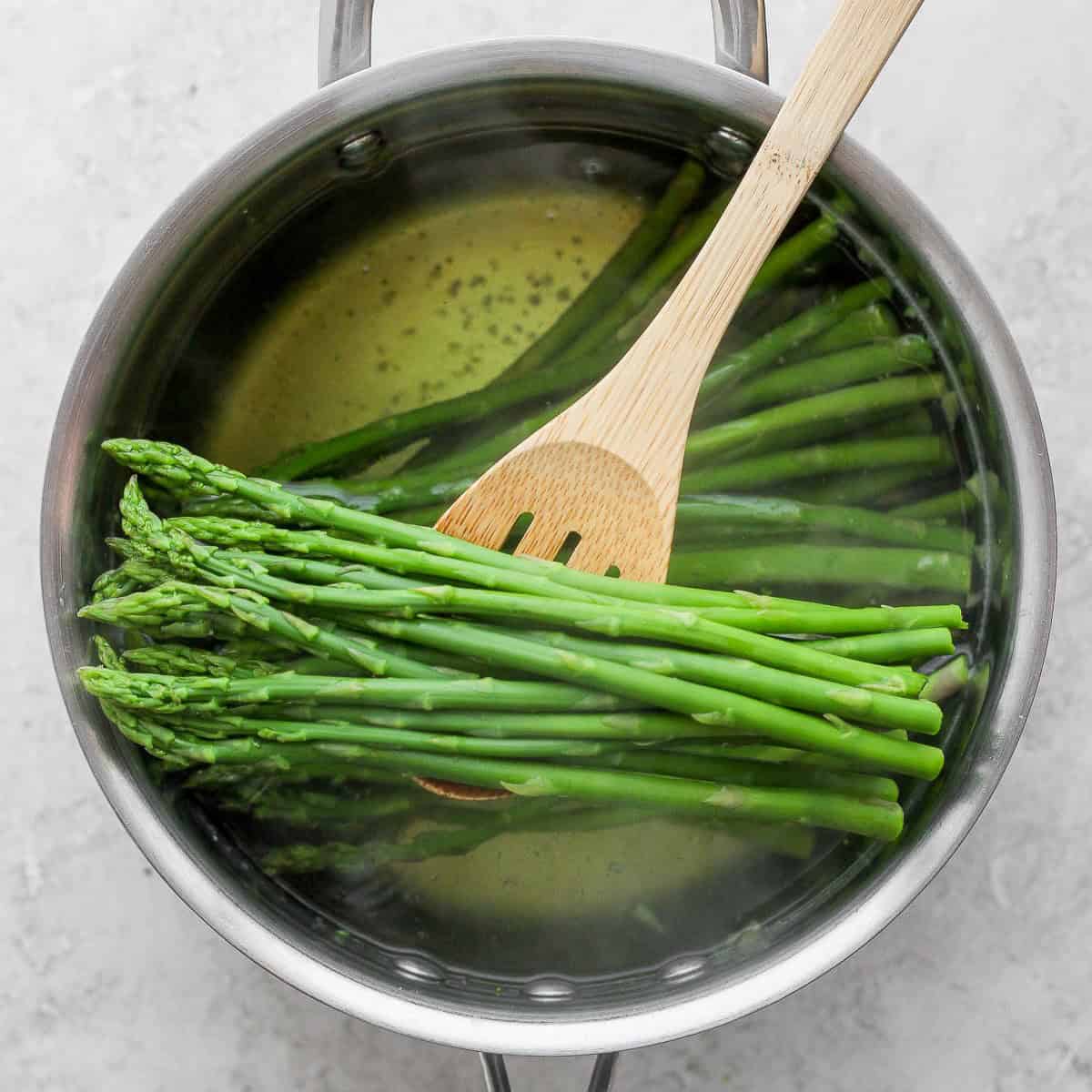 Wood spoon lifting veggies out of cooking water to show bright green color.