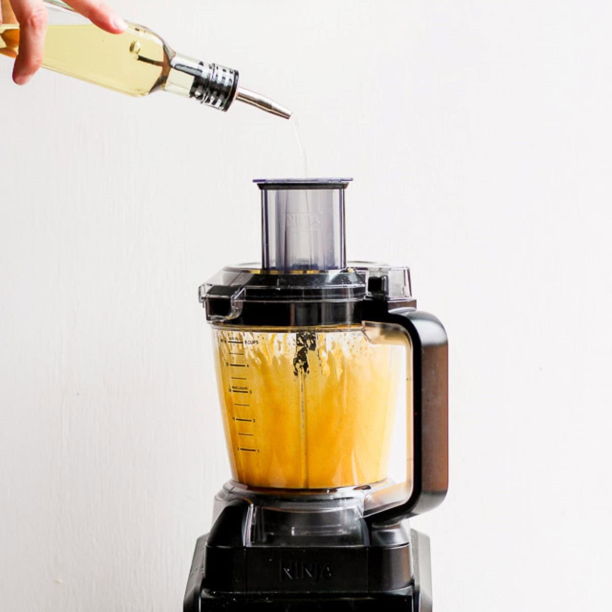 Food processor on with oil being poured in.