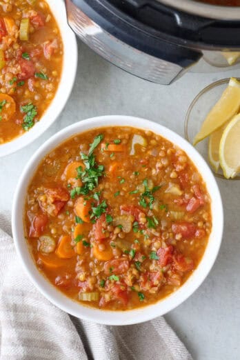 Hearty lentil soup in a bowl garnished with fresh herbs with pressure cooker nearby.
