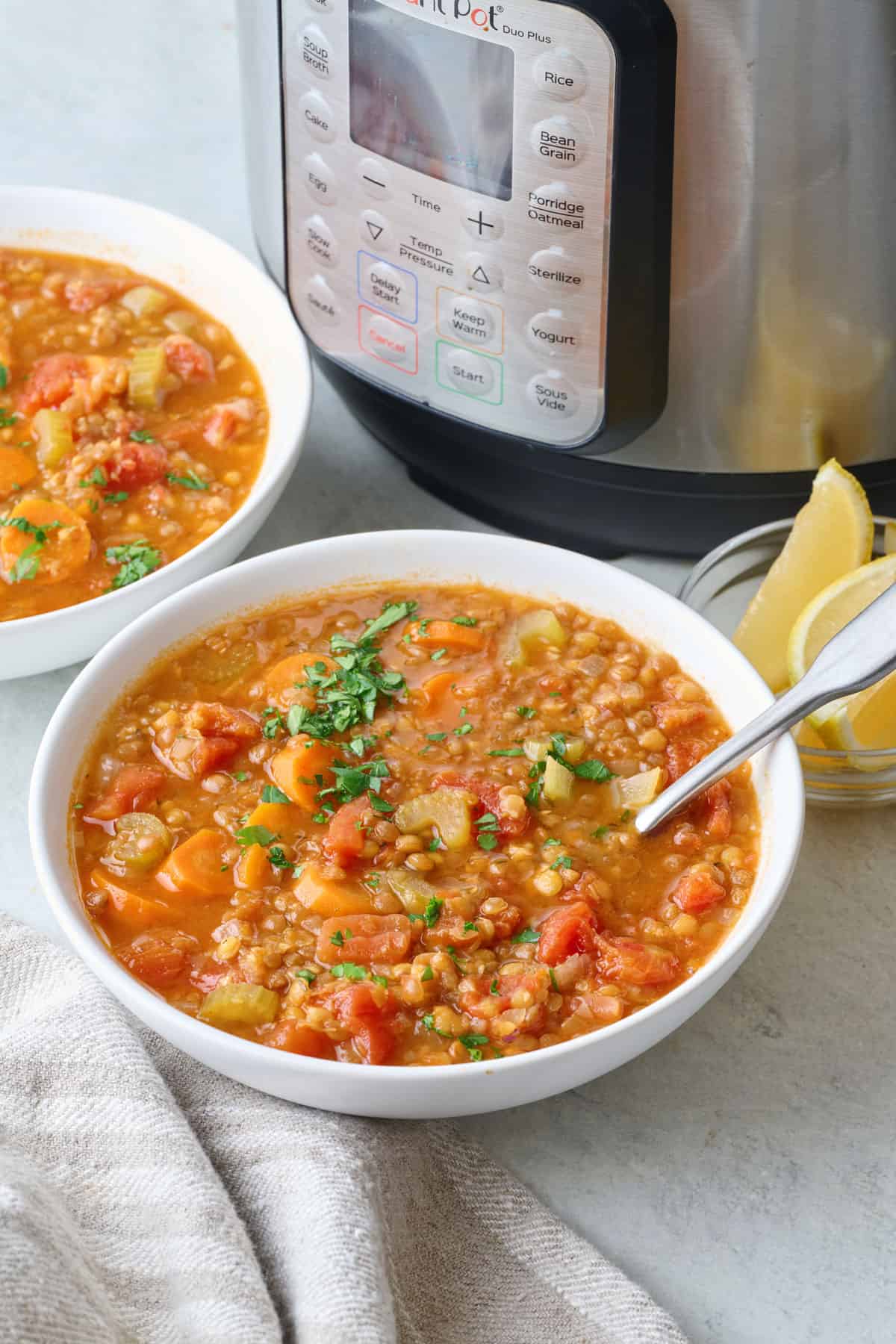 Two bowls of lentil soup with carrots and tomatoes with spoon dipped inside and Instant pot nearby.