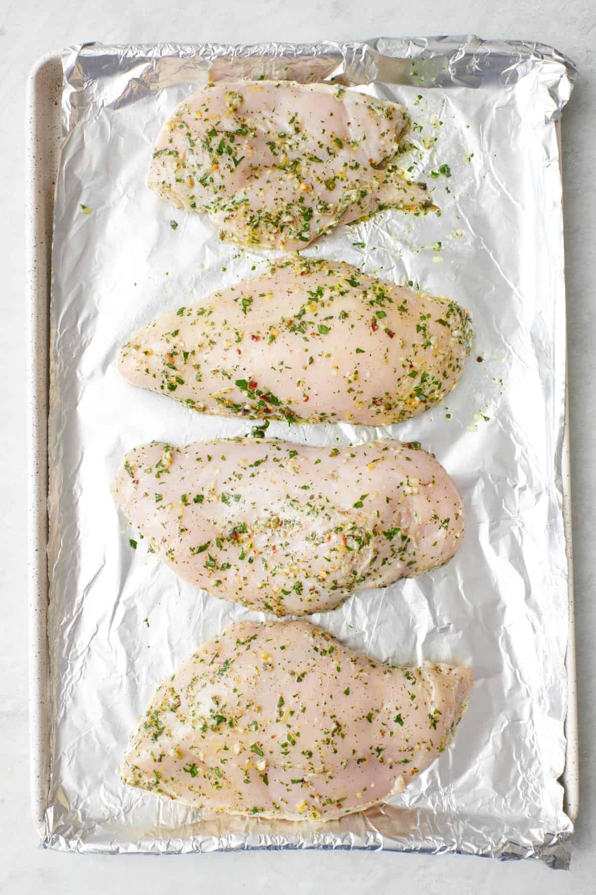 Seasoned chicken breasts on a foil line sheet pan before baking.