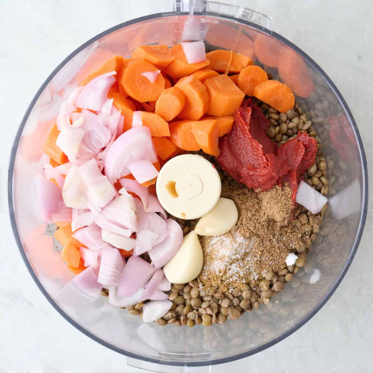 Chopped veggies, lentils, spices, and tomato paste in a food processor bowl.