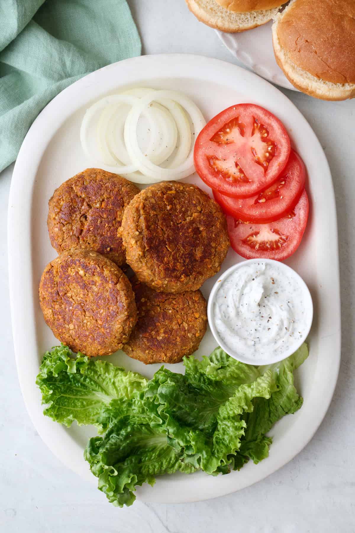 Homemade lentil burger patties on a platter with extra toppings around.