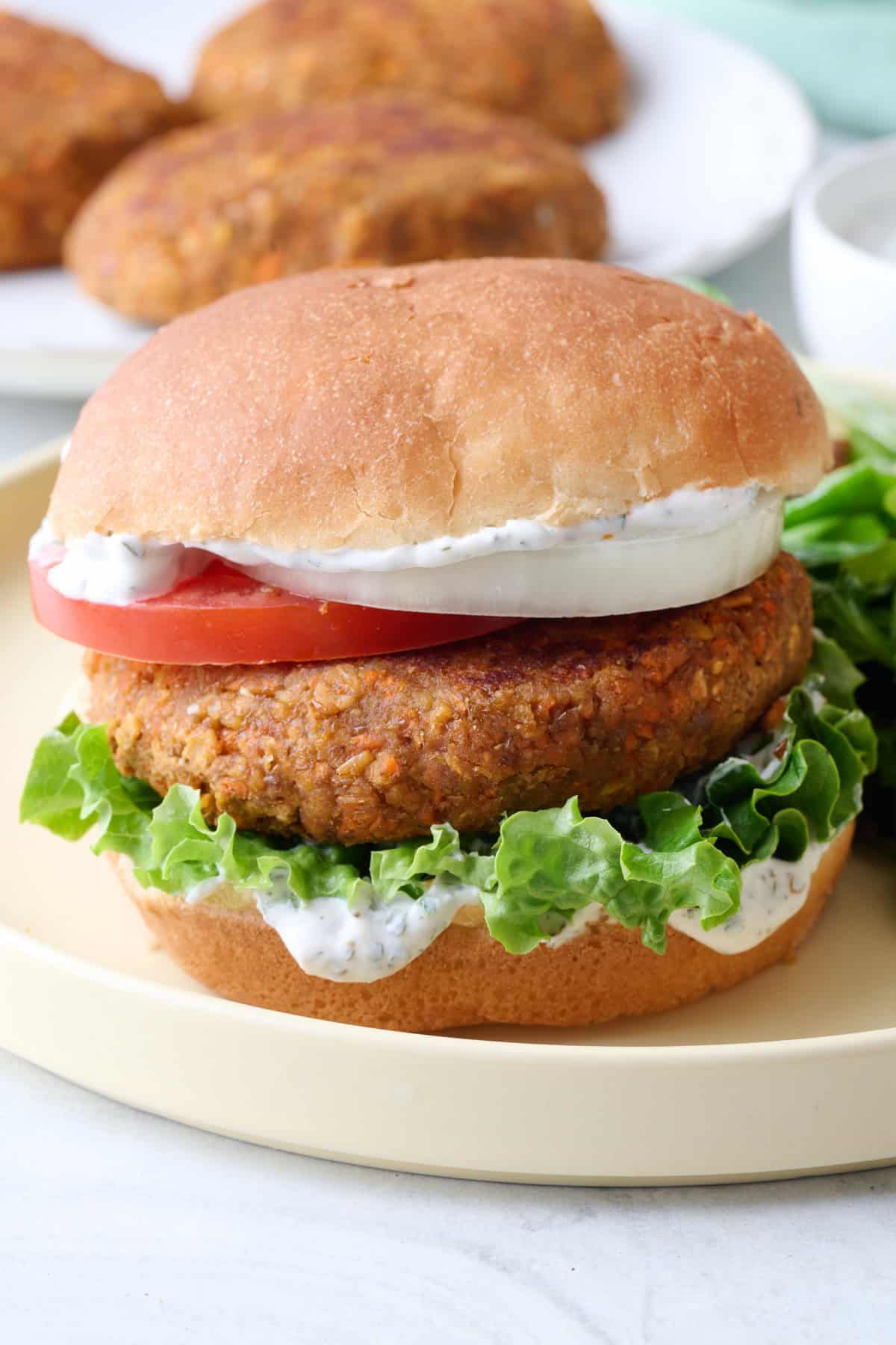 Thick and juicy lentil burger patty on a bun with sauce, lettuce, tomato, and onion.