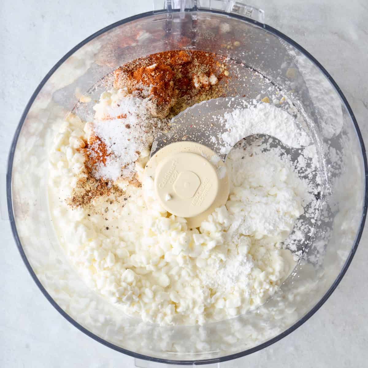 Cottage cheese, cornstarch, and seasonings in the bowl of a food processor.