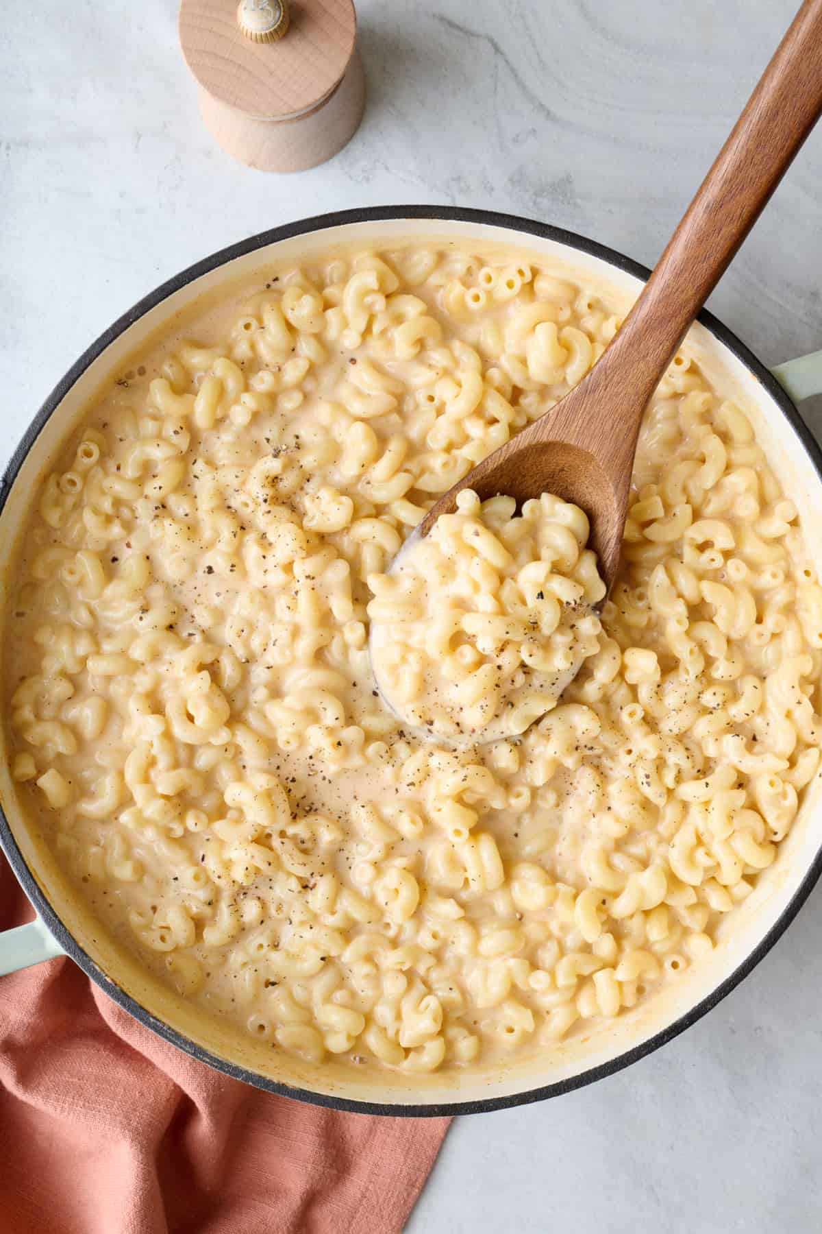 Cottage cheese macaroni and cheese in pot garnished with fresh ground black pepper, and a spoon dipped inside.