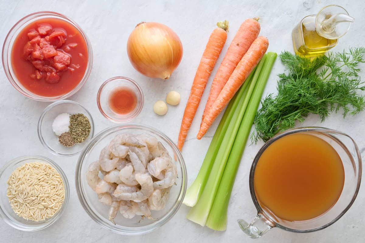 Ingredients for recipe before prepping: diced, tomatoes, salt, pepper, dried oregano, dry orzo, shrimp, red wine vinegar, garlic, onion, carrots, celery, fresh dill, broth, and oil.