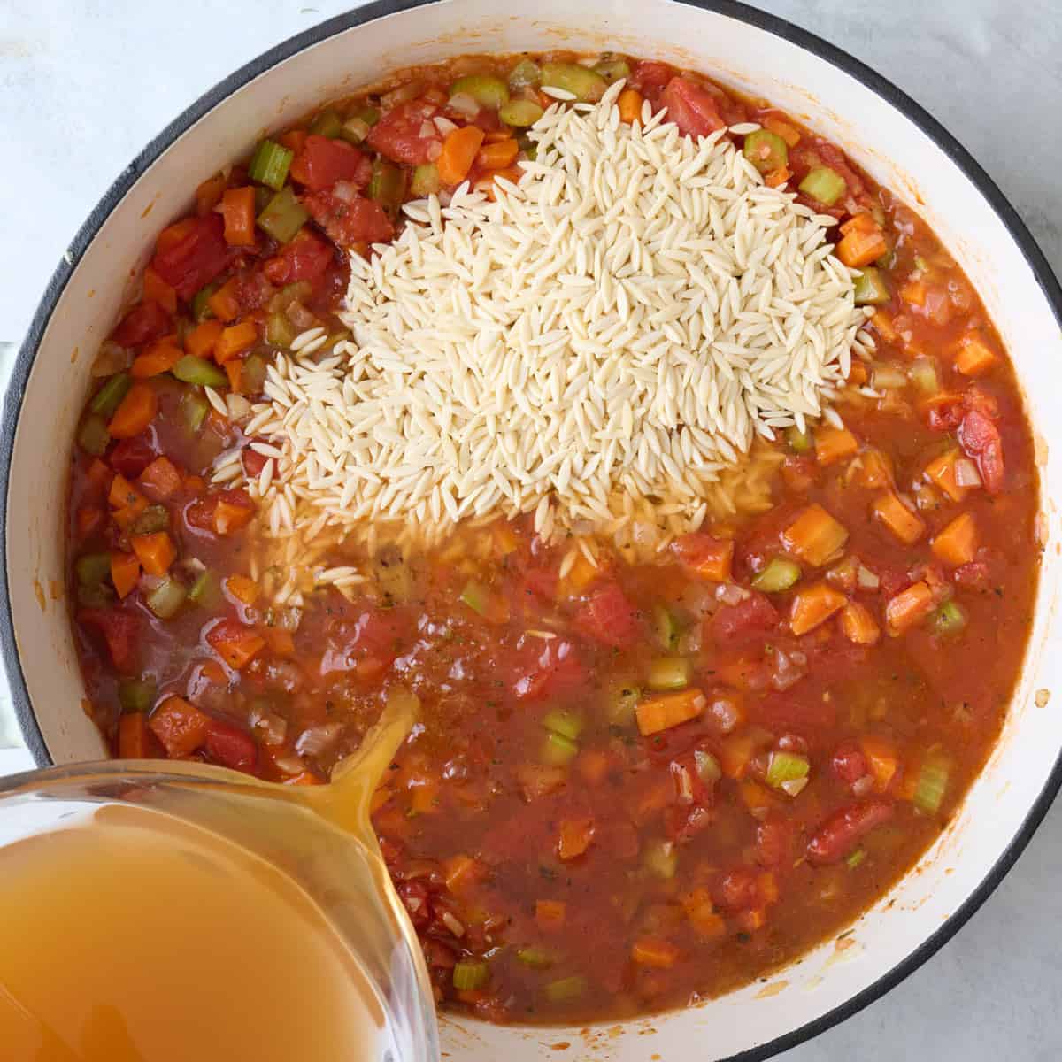 Orzo added to pot with broth being poured in.